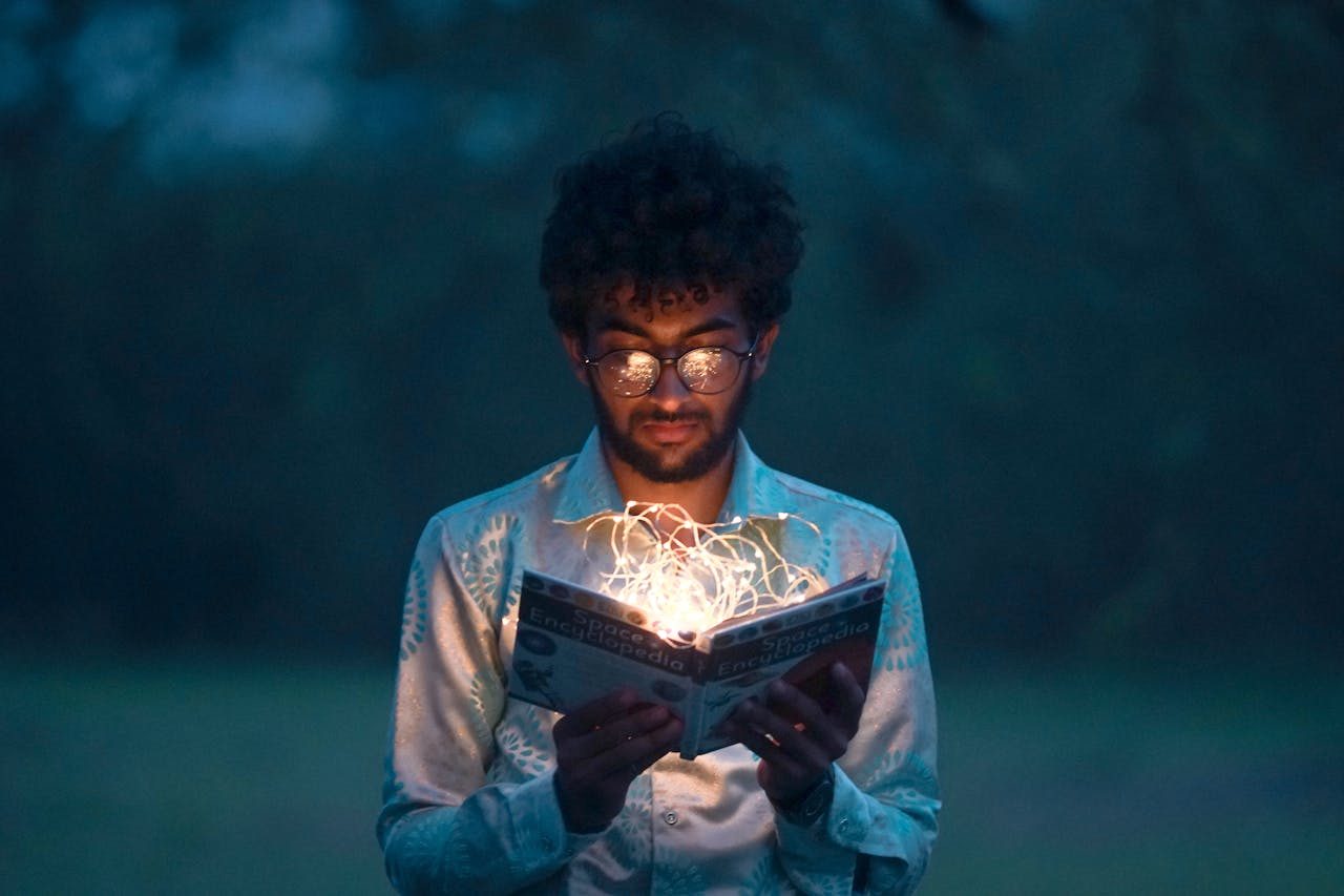 Services A man with glasses reads an illuminated book outdoors during twilight.
