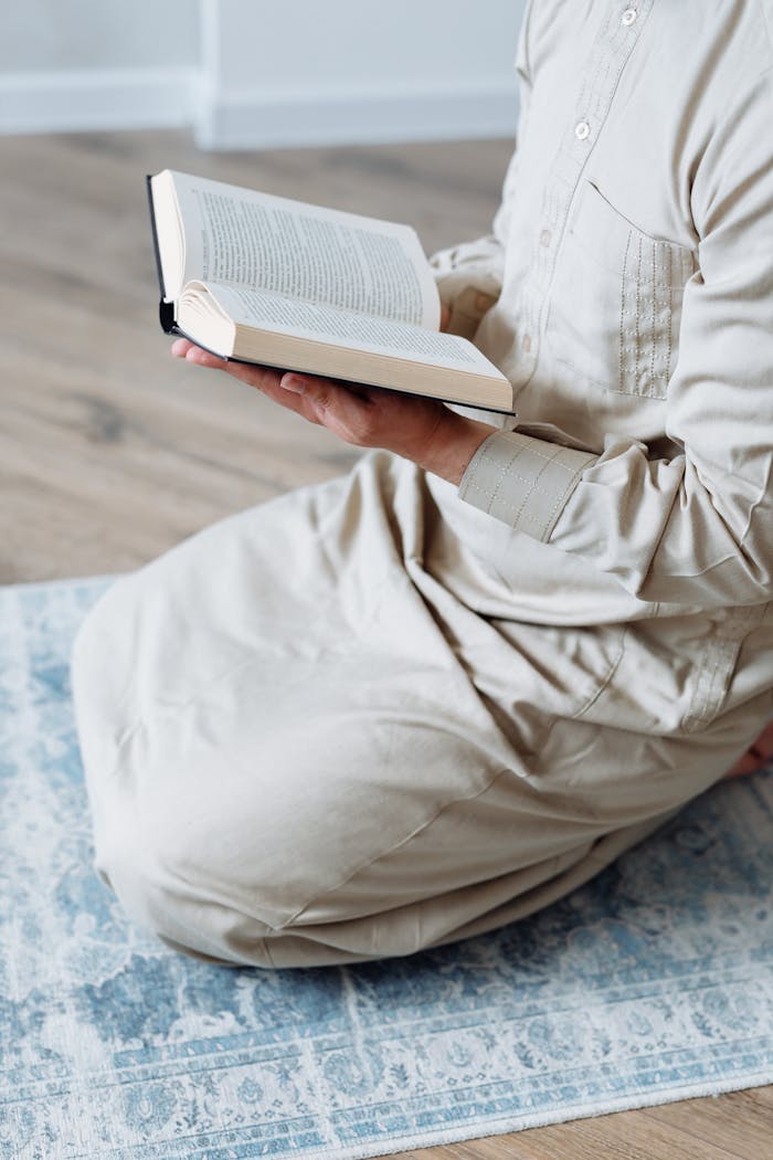 Services A person in traditional attire reading the Quran on a prayer mat indoors.